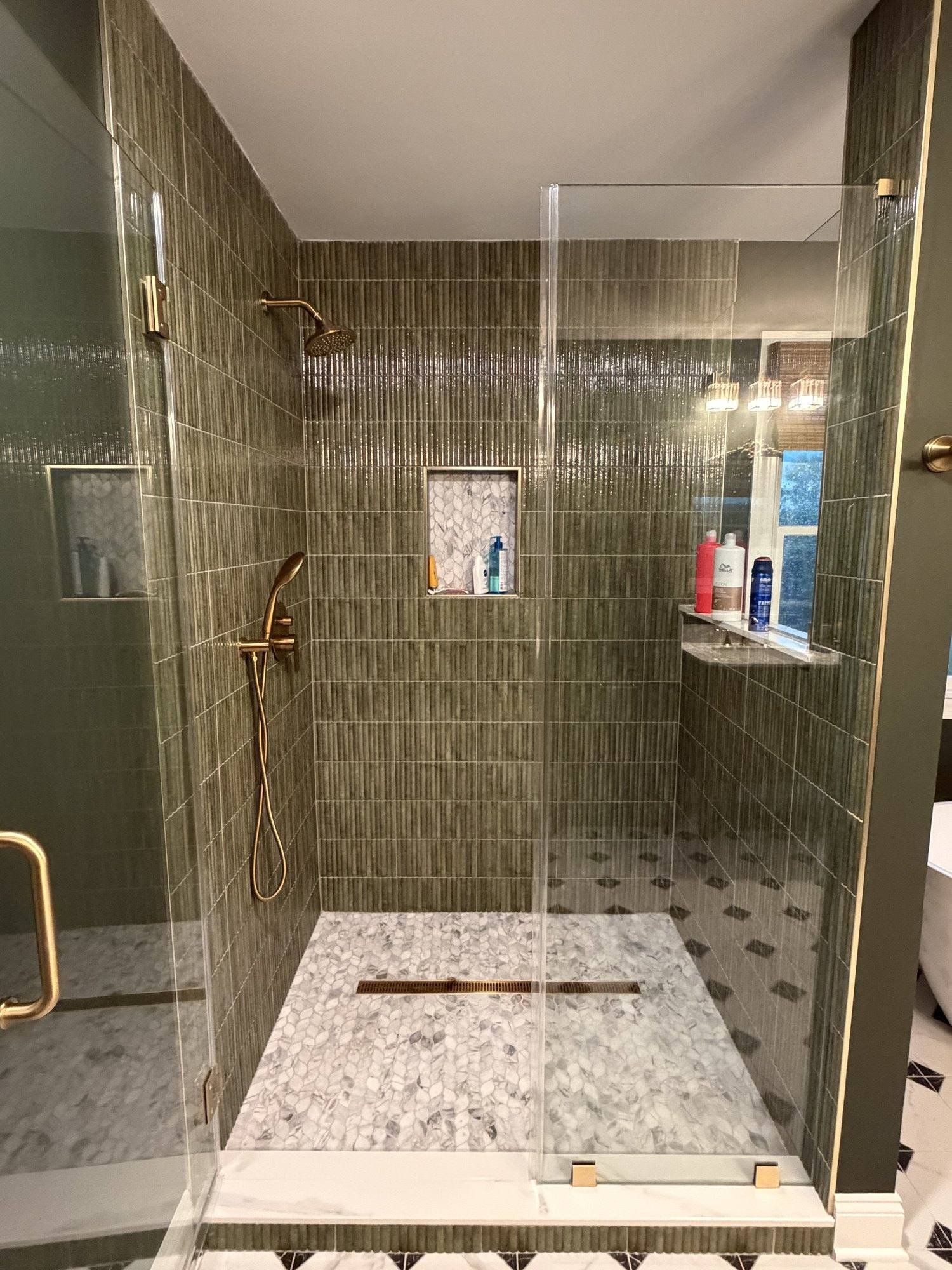 Frameless glass shower with brass fixtures and lit niche