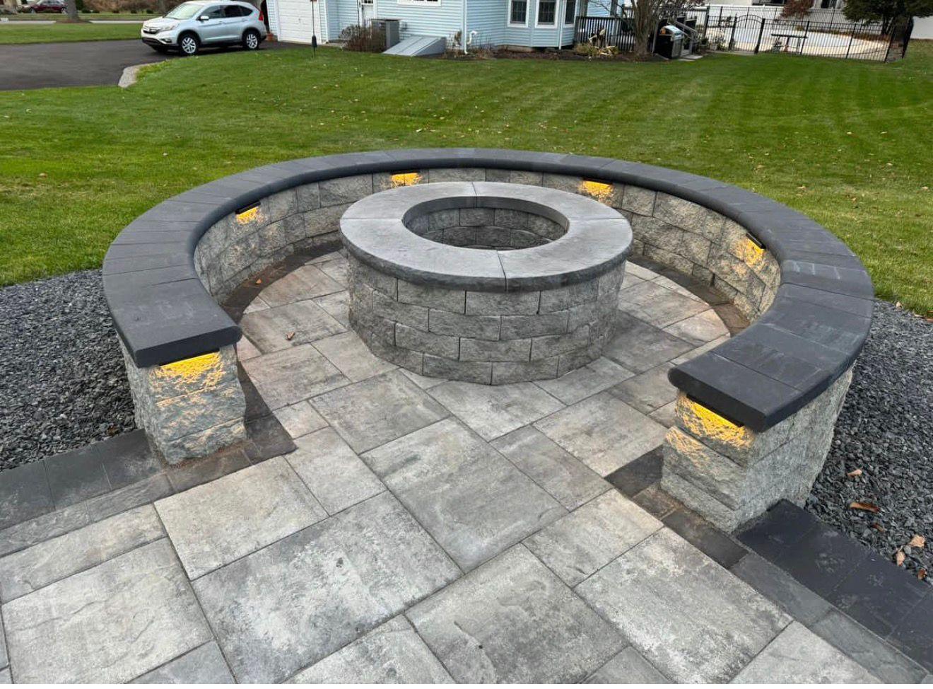 Circular stone fire pit with a curved seating wall and gray paver patio