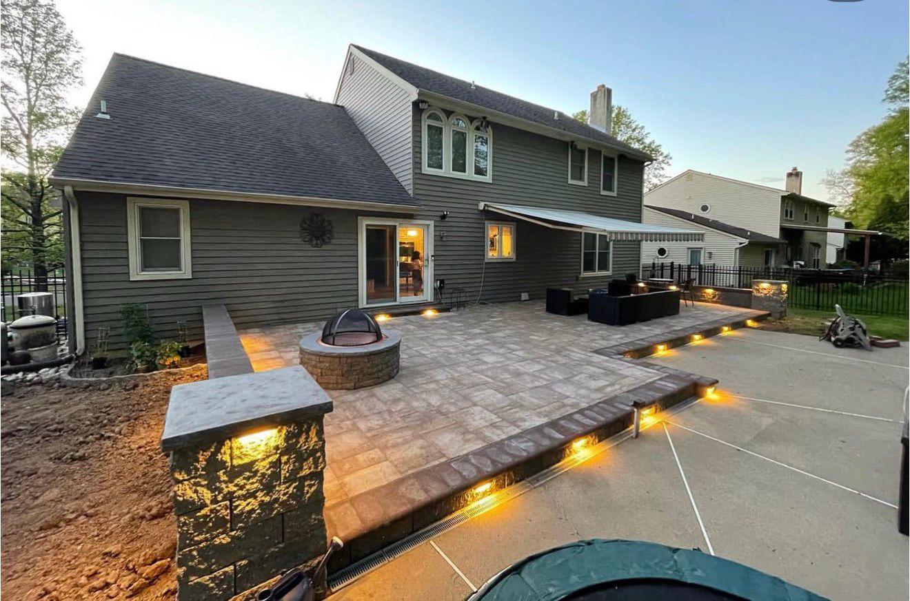 Raised paver patio with stone fire pit and LED step lighting at dusk